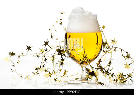 Volle kurze Glas helles Lagerbier, Pilsner Bier mit einem großen Kopf von Schaum und goldene Weihnachten Lametta auf weißem Hintergrund Stockfoto