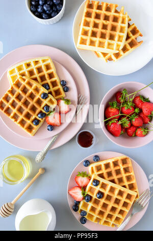 Belgische Waffeln mit Erdbeeren und Blaubeeren auf rosa Platte auf grau Holz- Hintergrund. Ansicht von oben. Platz kopieren Stockfoto