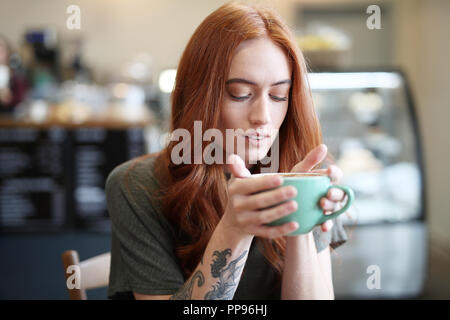 Redhead, weiblicher Single, sitzt in einem City Cafe mit einem heißen Getränk in einer Schale. Stockfoto