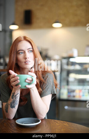 Redhead, weiblicher Single, sitzt in einem City Cafe mit einem heißen Getränk in einer Schale. Stockfoto