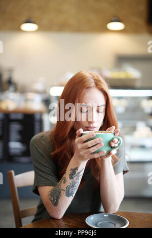 Redhead, weiblicher Single, sitzt in einem City Cafe mit einem heißen Getränk in einer Schale. Stockfoto