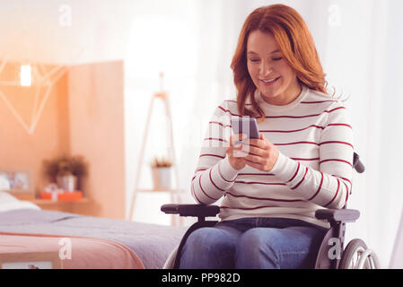 Positive wheelchaired Frau mit Smartphone Stockfoto
