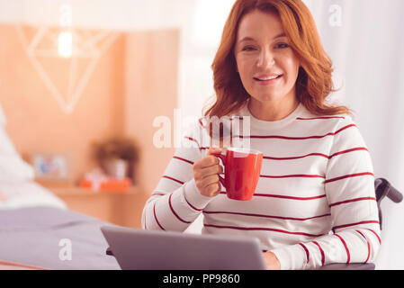 Freudige behinderte Frau trinkt Kaffee Stockfoto