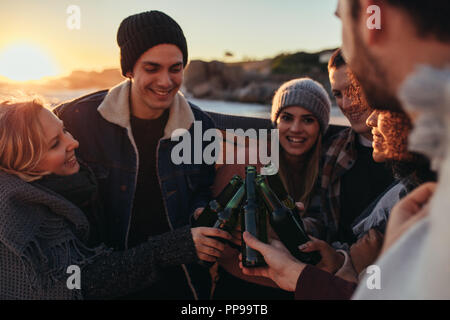 Gruppe von multi-ethnischen Jugendliche toasten Bier am Strand. Freunde Ausgabe Zeit zusammen am Strand mit ein paar Drinks während des Sonnenuntergangs. Stockfoto