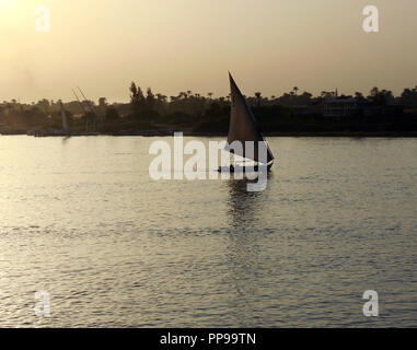 Ein einsamer Feluke Segeln auf dem Nil, vermutlich auf dem Weg nach Hause, als die Sonne auf den mächtigen Nil in Ägypten. Stockfoto