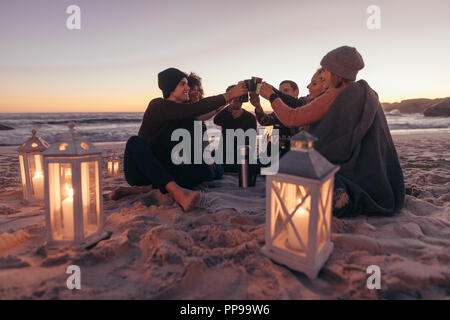 Gruppe von Jugendlichen zusammen am Strand sitzen, Kaffee rösten auf warmen Abend. Freunde feiern am Strand mit Kaffee. Stockfoto