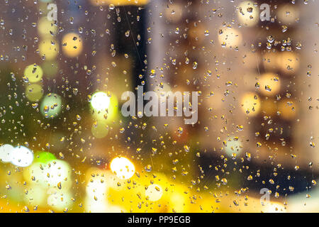 Herbst Regenwetter - Ansicht von unscharfen nachts beleuchteten Apartment Gebäude durch das Haus Fenster mit Regentropfen (Fokus auf der Regen fällt auf die Gl Stockfoto