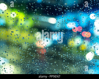 Herbst Regenwetter - Ansicht von unscharfen Nacht Lichter der Stadt durch das Haus Fenster mit Regentropfen (Fokus auf die Regentropfen auf dem Glas) Stockfoto
