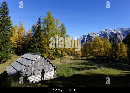 Silhouette der Junge vor einem hölzernen urige Hütte auf der Alm auf einer schönen Herbstnachmittag, umgeben von den Julischen Alpen, Slowenien, Vršič Stockfoto