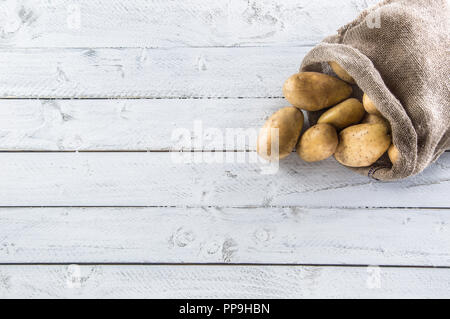 Reifen Kartoffeln in sackleinen Sack frei liegend auf Holzbrett. Stockfoto