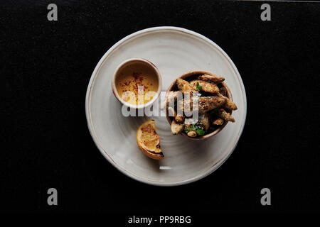 Köstlicher knuspriger Weißfisch in einer Schüssel auf weißem Teller mit gebratenem Zitronenkeil und leckerer Limonen-Hollandaise-Sauce im coolen Londoner Restaurant Stockfoto