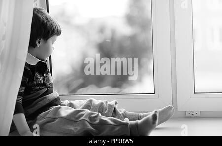 Der kleine Junge ist ein Buch zu lesen. Das Kind sitzt am Fenster ein Stockfoto