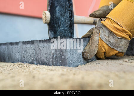 Handwerker installieren von Pflastersteinen oder Backsteine in der Nähe zu sehen, der seine behandschuhten Hände halten ein Hammer Sie auf einer sand Basis in einem niedrigen Winkel tamp c Stockfoto