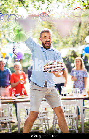 Mann springen mit einem Kuchen auf einer Familienfeier oder eine Gartenparty außerhalb. Stockfoto