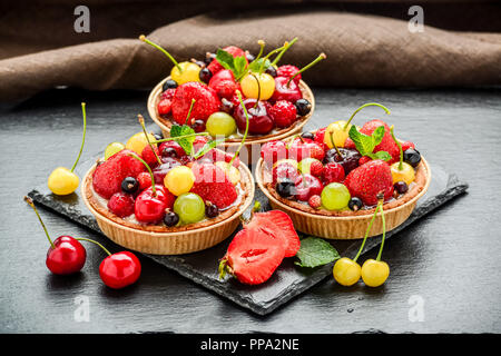 Berry Törtchen mit Blaubeeren, Himbeeren, Kiwi, Erdbeeren, Mandelflocken in Puderzucker. Stockfoto