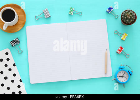 Notebook mit leeren Seiten und andere Büroartikel über Mint blau Büro Schreibtisch Tabelle öffnen. Ansicht von oben Stockfoto
