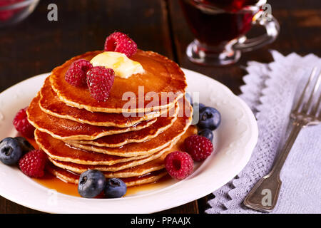 Pfannkuchen mit frischen Beeren und Ahornsirup auf hölzernen Tisch Stockfoto