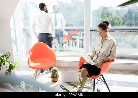 Portrait von zwei Personen im Wartezimmer der modernen Büro-, Fokus auf Frau lesen Magazin in hellen orange Stuhl Stockfoto
