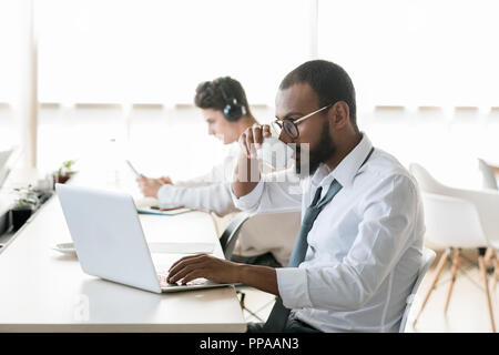 Seitenansicht Portrait von bärtigen des Nahen Ostens Geschäftsmann Kaffee trinken bei der Arbeit und mit Laptop im Open Office, kopieren Raum Stockfoto