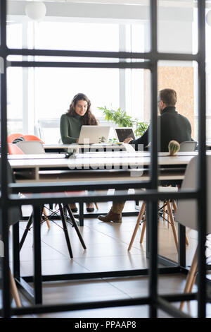 Portrait von jungen lateinamerikanischen Frau lächelnd, während am Computer in Open Space Office arbeiten Stockfoto