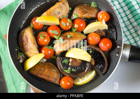 Pilze und Tomaten, in einer flachen Pfanne gebraten Rühren, Pan, mit frisch gehackter Petersilie und Zitrone Keile garniert Stockfoto
