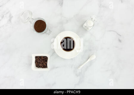 Schwarzen Kaffee in eine Tasse, Weißzucker, gemahlenen Kaffee und Kaffeebohnen auf weißem Hintergrund. Stockfoto