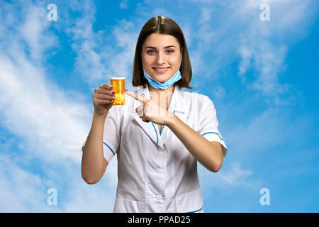 Frau Doktor mit Pillen auf Himmel Hintergrund. Ziemlich medizinischer Arbeiter Holding orange Flasche Medikation. Menschen, die Medizin, die Pharmakologie. Stockfoto