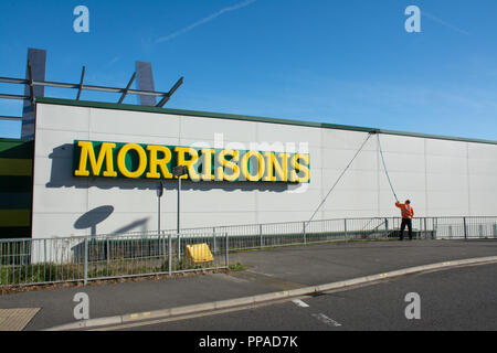 Westgate Retail and Leisure Park - Außenansicht des Morrisons Supermarktes mit Mann, der die Außenwand mit langem Pol-Rakel reinigt, Aldershot, Großbritannien Stockfoto
