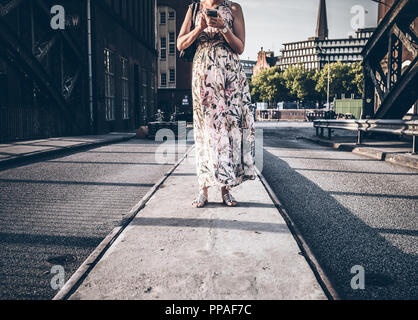 Frau im Sommerkleid stehen auf der Straße mit Hilfe von Phone Stockfoto