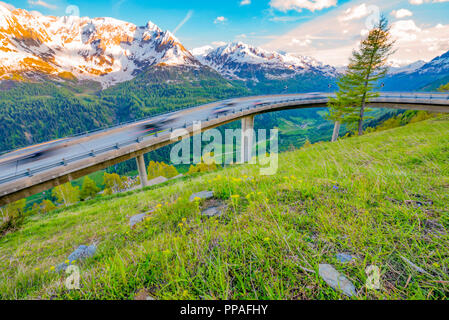 Datenverkehr über eine gekrümmte Mountain Road Bridge und die schneebedeckten Berge in der Schweiz. Stockfoto