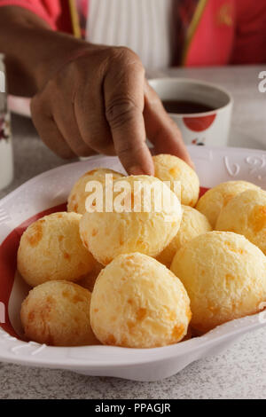 Eine weibliche Hand, denn ein Käse, Brot (auch bekannt als Pao De Queijo) aus dem Korb; typisch brasilianisches Frühstück Szene. Selektive konzentrieren. Stockfoto