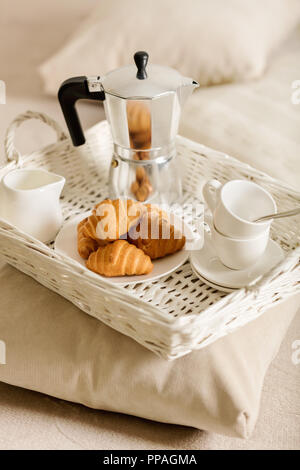 Frühstück im Bett. Auf einem weißen Korbsesseln Fach gibt es eine Kaffeemaschine, Kaffee weißen Tassen und Croissants. Selektive konzentrieren. Stockfoto