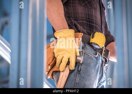 Erste Baustelle Konzept Foto. Kaukasische Arbeiter mit Tools Riemen großen Hammer und Maßband. Closeup Foto. Stockfoto