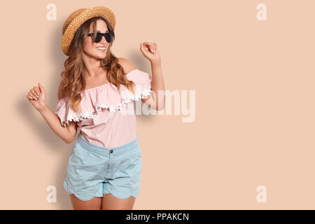Studio shot zufrieden adorable Weiblichen im Sommer Bekleidung, hat positiven Ausdruck, wirft gegen Studio Hintergrund mit Platz für ihre advetisem kopieren Stockfoto