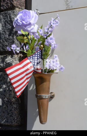 Patriotische Grab Denkmal mit allen Wetter Blau Violett künstliche Blumen und die amerikanische Flagge auf mausoleum Wand Stockfoto