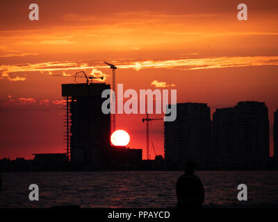 Industrielle Baustelle bei Sonnenuntergang mit Kran auf ein Büro oder Gebäude im Bau Silhouette gegen einen bunten Roter Himmel mit Sonne und p Stockfoto