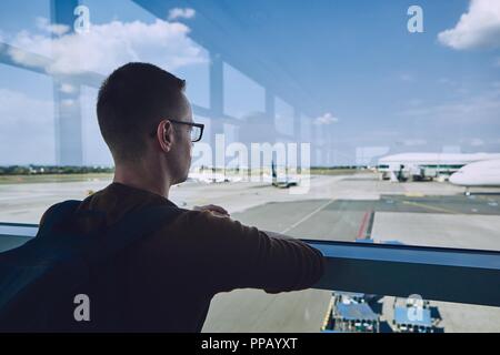 Kleinen Passagier am Flughafen warten und schauen durch das Fenster zum Flugzeug. Stockfoto