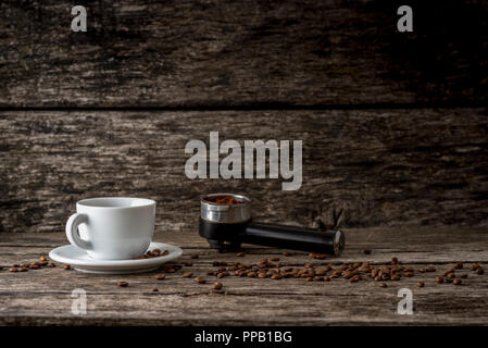 Weiße Tasse Kaffee, verstreute Kaffeebohnen und gemahlenen Kaffee in Metall Maßnahme einer Kaffeemaschine auf einer rustikalen texturierte Holzbretter mit der Stockfoto