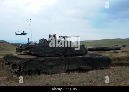 Ein 12 Combat Aviation Brigade AH-64 Apache Kampfhubschrauber und eine M1A2 Abrams Panzer, die zu Charlie Company, 2nd Battalion, 5th Cavalry Regiment, 1st Armored Brigade Combat Team, 1.Kavallerie Division vorzubereiten während einer kombinierten Waffen live fire Übung mit US-amerikanischen und der georgischen Streitkräfte in Wasiani, Georgia, Feuer August 14, 2018. Edle Partner 2018 ist eine georgische Streitkräfte und US-Armee Europa kooperativ-led bei der Verbesserung der Bereitschaft und der Interoperabilität von Georgia, USA und anderen teilnehmenden Nationen. Stockfoto