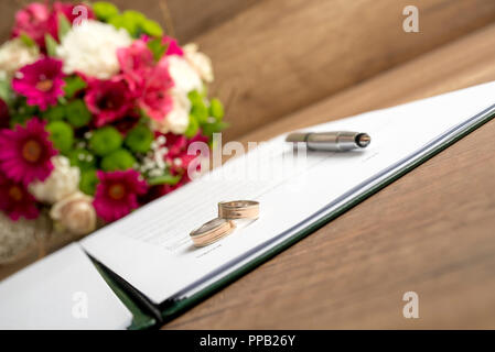Hochzeit Registrieren mit Stift, Braut und Bräutigam Ringe und Strauß mit frischen Blumen auf einem Holztisch. Stockfoto