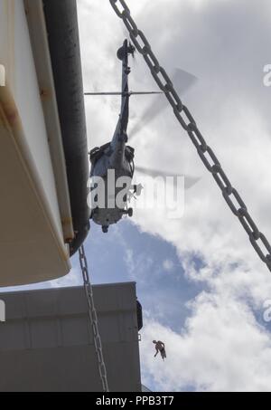 Segler für die Beseitigung von Explosivstoffen Mobile Einheit (EODMU) 5, Hubschrauber Meer Combat Squadron 25 und Australische Soldaten einer trainingspuppe während eines Besuchs, Board, Durchsuchung und Beschlagnahme Betrieb an Bord der maritimen Vorpositionierung ship USNS 1st Lieutenant Jack Lummus (T-AK 3011) während der Ausbildung "Pyrocrab' bei Apra Harbor, Guam, 15 August, 2018 Hebezeug befestigt. Pyrocrab ist eine Biennale Ebene der Ausbildung, die auf die Stärkung der Beziehungen und die Verbesserung der Interoperabilität zwischen der U.S. Navy und der australischen Streitkräfte konzentriert. EODMU-5 ist zum Kommandanten, Task Force 75, die primäre Expedit zugeordnet Stockfoto