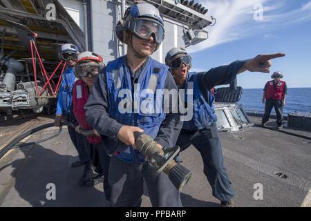 Meer von Japan (20. August 2018) Seaman Blake Hendrickson, rechts, vom Largo, Florida, leitet ein löschschlauch Team auf dem Flugdeck der Ticonderoga-Klasse geführte-missile Cruiser USS Antietam (CG54) bei einem Crash und Bergung Ausbildung bohren. Antietam ist auf Patrouille in den USA 7 Flotte, der Unterstützung der Sicherheit und Stabilität in der indopazifischen Region. Stockfoto