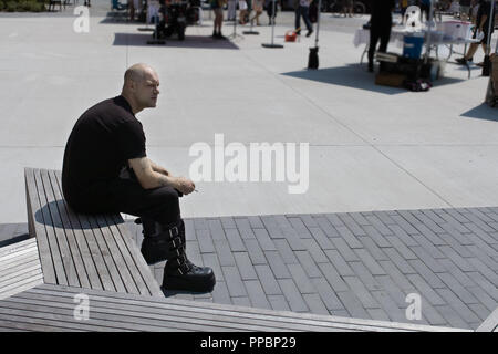 Junger Mann Gothic gekleidet, Sitzen und smocking eine Zigarette auf dem Platz Markt in Stratford, Ontario. Stockfoto