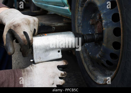 Mann mit dem pneumatischen Säsystem ändern Reifen auf dem Auto | Handschuhe | Rost Stockfoto