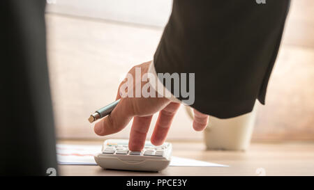 Unternehmer oder Steuerberater wichtige finanzielle Berechnung auf eine manuelle desk top Rechner, Low Angle View zwischen seinen Arm und Körper der paperw Stockfoto