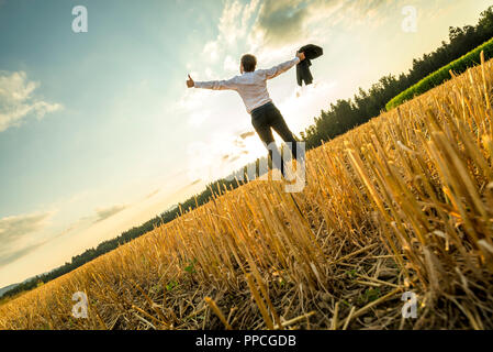 Rückansicht eines erfolgreichen Junge Unternehmer stehen am Feld mit weit offenen Armen und sah in den Himmel. Stockfoto