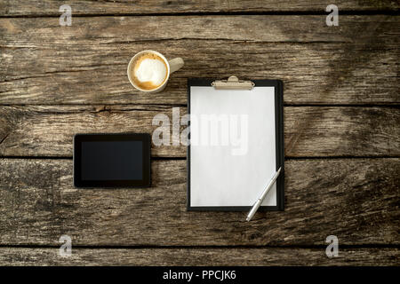 Ansicht von oben von texturierten rustikal Holz- Studie oder Büro Schreibtisch mit einem leeren weißen Blatt Papier, digital Tablet und Tasse frischen Kaffee. Stockfoto