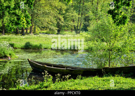 Holz Boot ist die Landung in der Nähe der Ufer des Teiches. Üppigen Laub sind im ruhigen Wasser Oberfläche reflektiert. Stockfoto