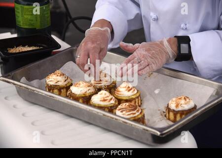 Kulinarische Mannschaften von der US Coast Guard, der U.S. Navy und der Royal Canadian Navy in der kochwettbewerb "Galley Wars' bei Los Angeles Flotte Woche in San Pedro, Kalifornien, Sept. 3, 2018 konkurrierte. Petty Officer 3. Klasse Melissa Northrop, Petty Officer 2nd class Derek Nguyen, und Petty Officer 1st Class Michael Allen, Coast Guard kulinarische Spezialisten der Coast Guard Cutter Alert, gewann die Koch - weg. Starkoch Robert Irvine verkündete die Sieger und hinten Adm. Daniel Dwyer, Commander, Carrier Strike Group Neun, präsentierte die Coast Guard Team mit dem ersten Platz ausgezeichnet, eine geschnitzte 2018 LA Stockfoto