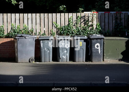 Schwarz wheelie Bins in einer Zeile auf Straßen mit Hausnummern auf der Vorderseite gedruckt Warten bin Männer zu sammeln Stockfoto